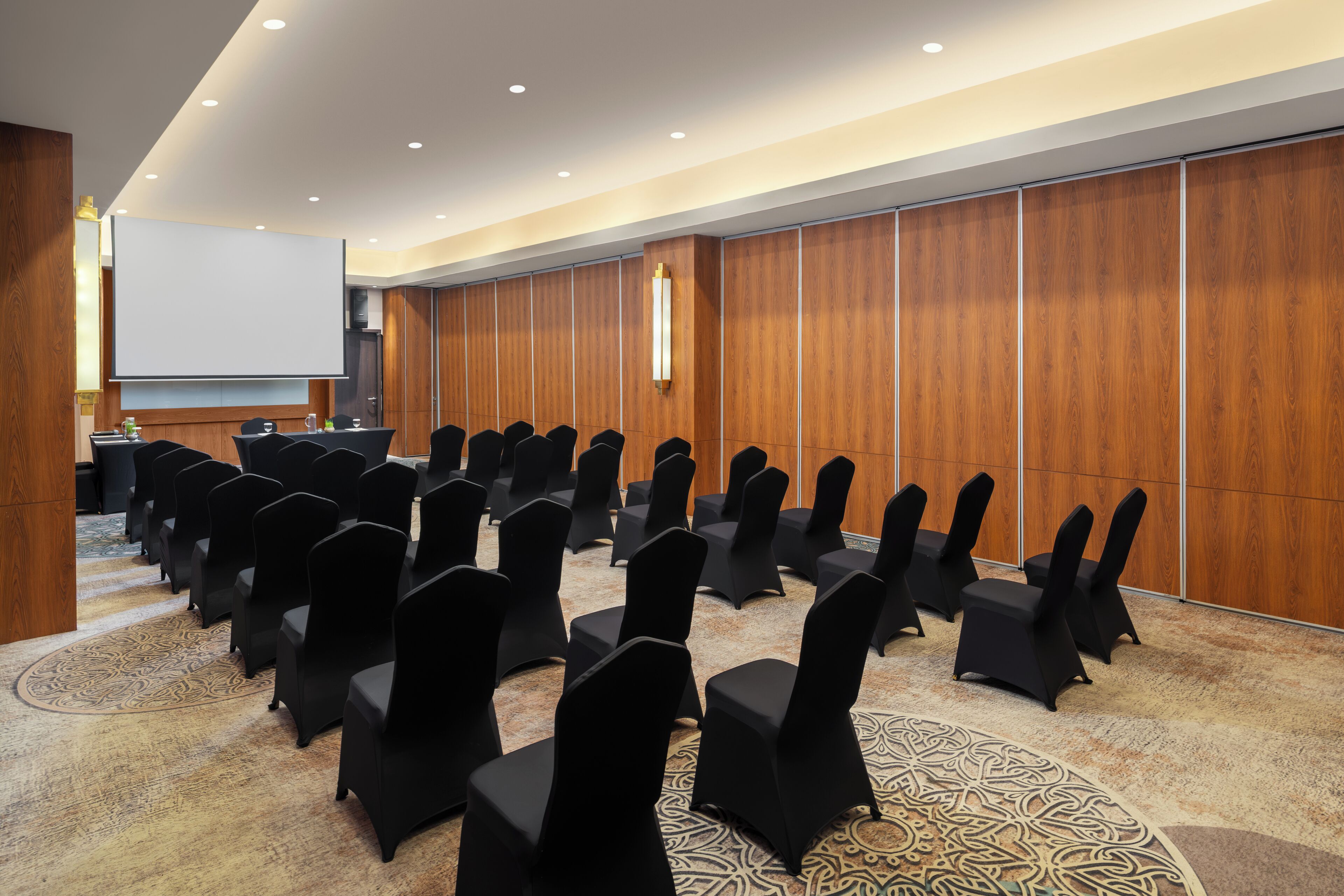 Un salón de conferencias con filas de sillas, una pantalla de proyector y un atril.