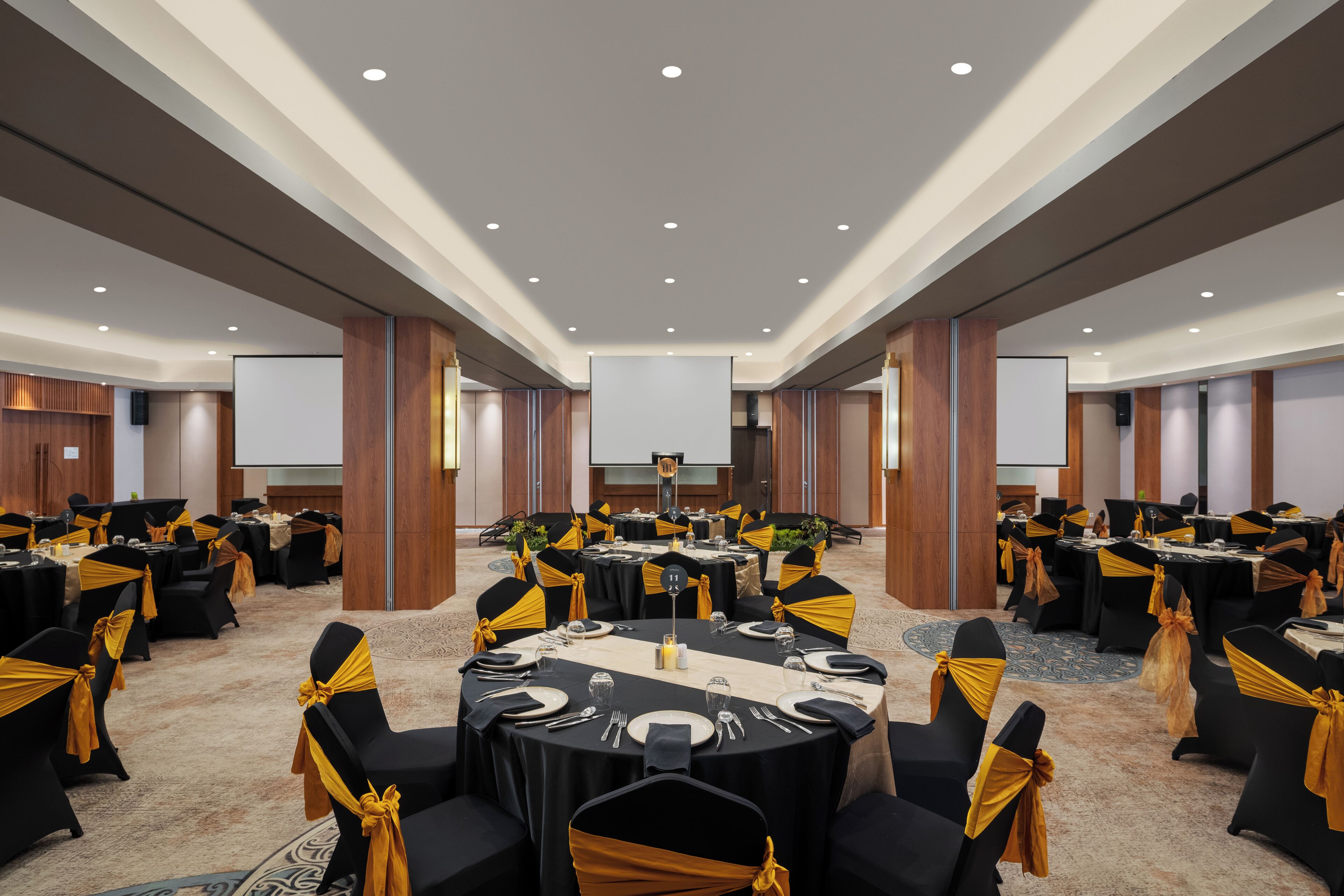 A large conference room with round tables, black chairs with gold sashes, and a projector screen at the front.