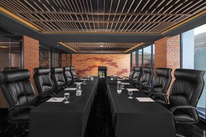 A conference room with a long table, black leather chairs, and a brick wall with a mosaic design.