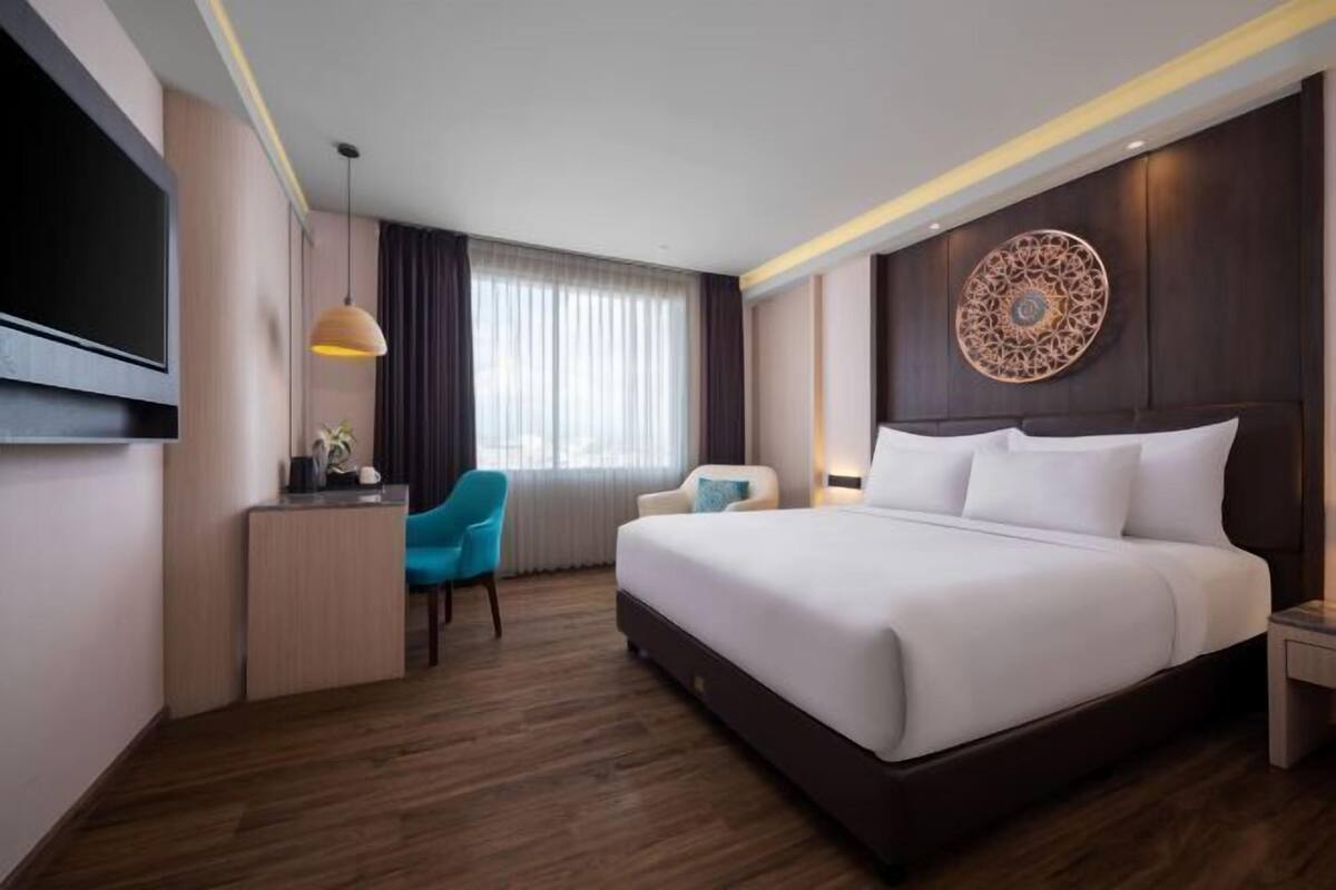 A hotel room with a large bed, a desk with a chair, a TV, and a decorative wall piece.