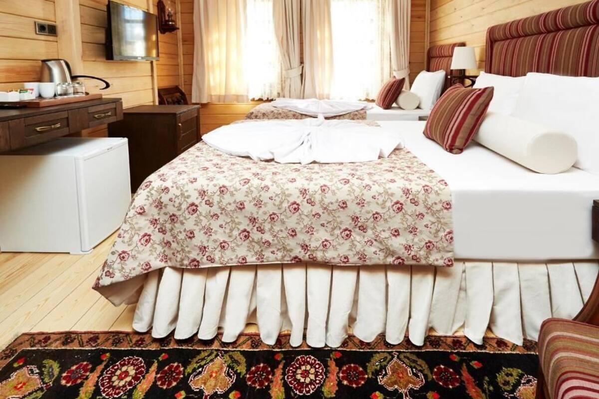 Een knus ingerichte kamer met een bed, een bureau, een televisie en een raam met gordijnen.