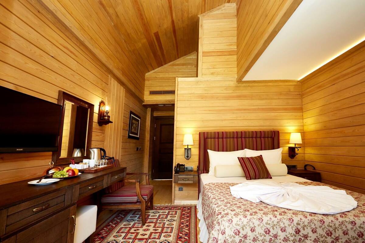 Een kamer met houten lambrisering, een bed, nachtkastje, lamp en een flatscreen-televisie.