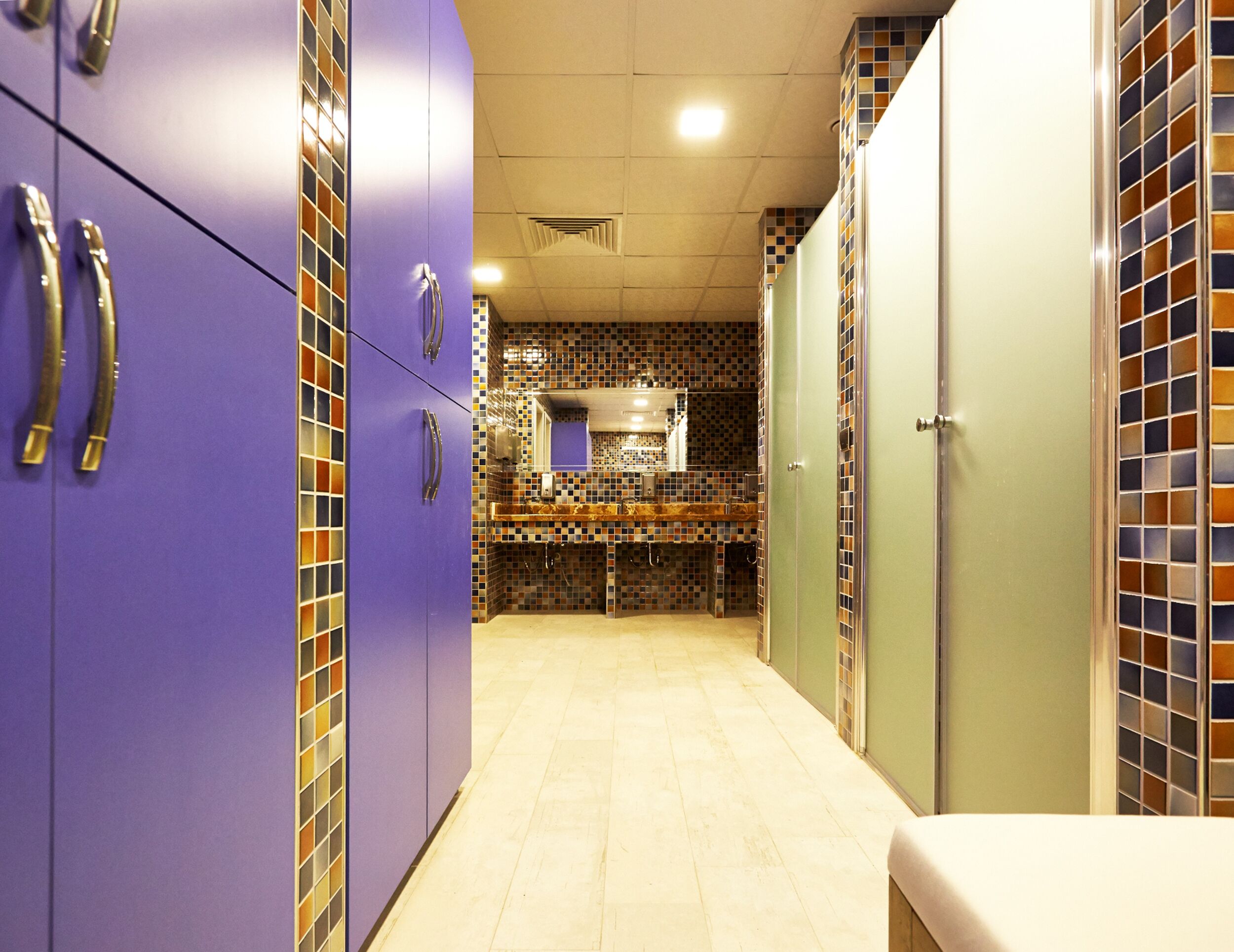 A narrow hallway with purple lockers, a tiled backsplash, and a light-colored floor.