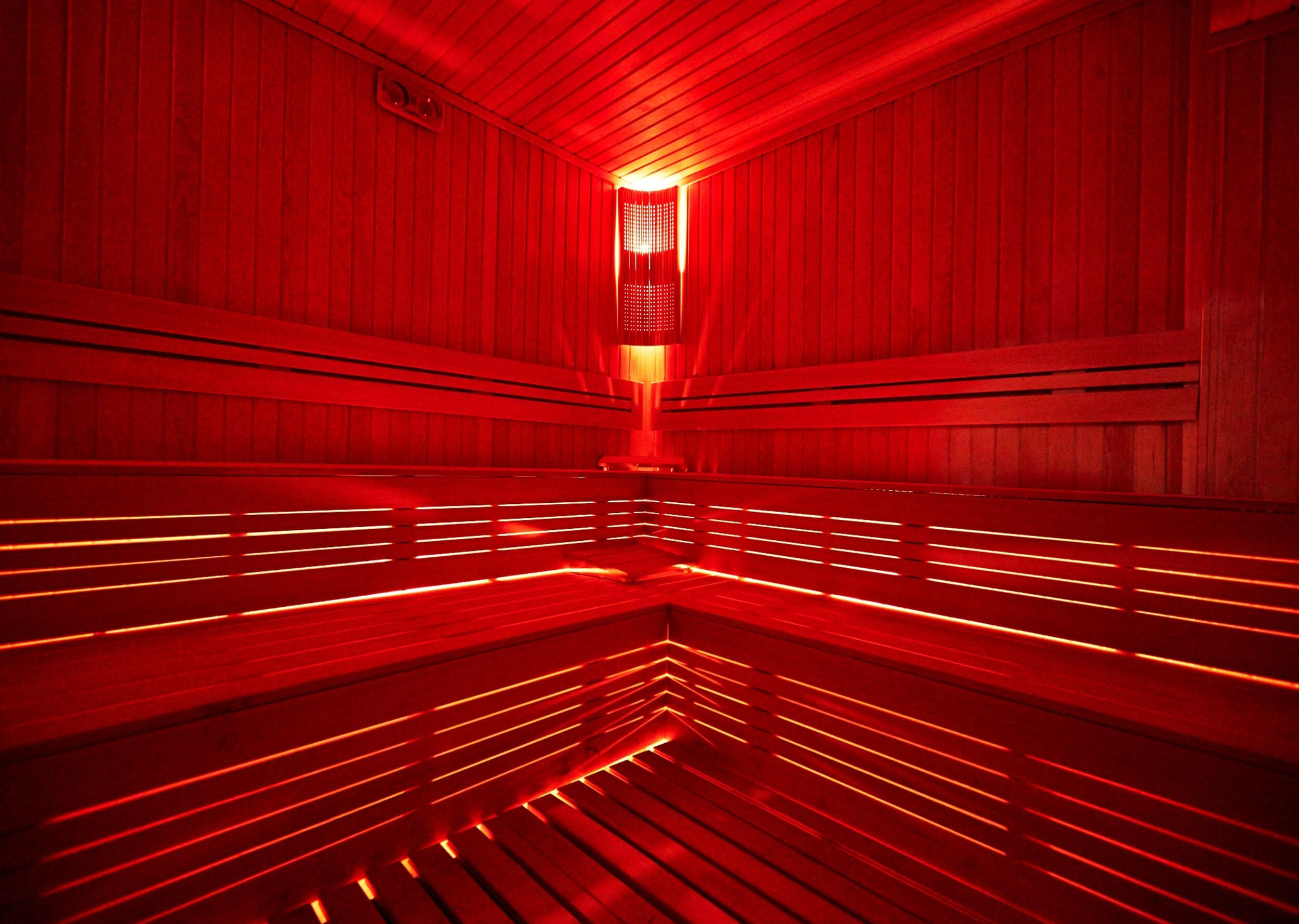 A sauna with wooden benches and red lighting.