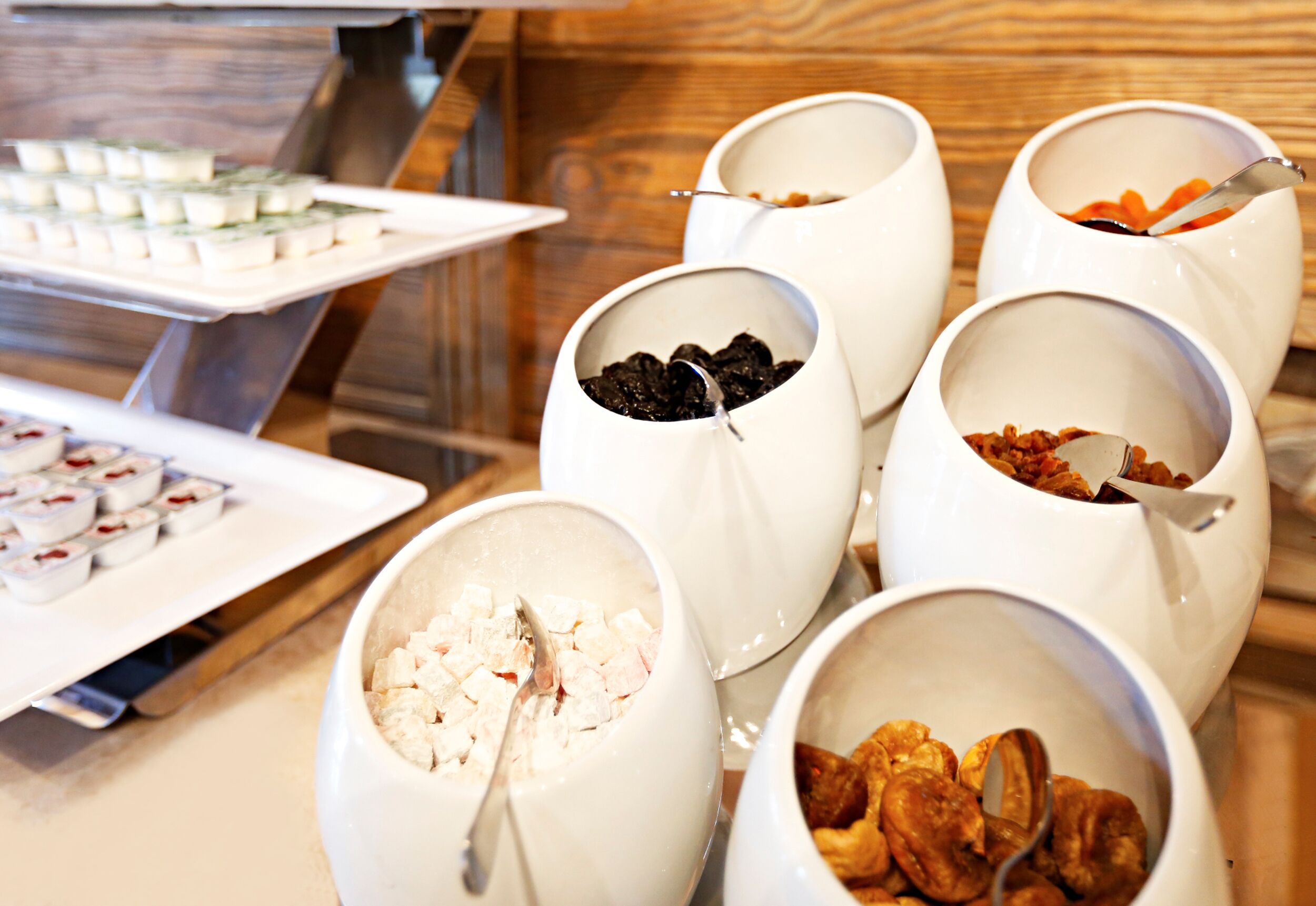 Un buffet proposant divers aliments présentés dans des bols blancs, notamment ce qui semble être des céréales, des noix et, peut-être, des fruits.
