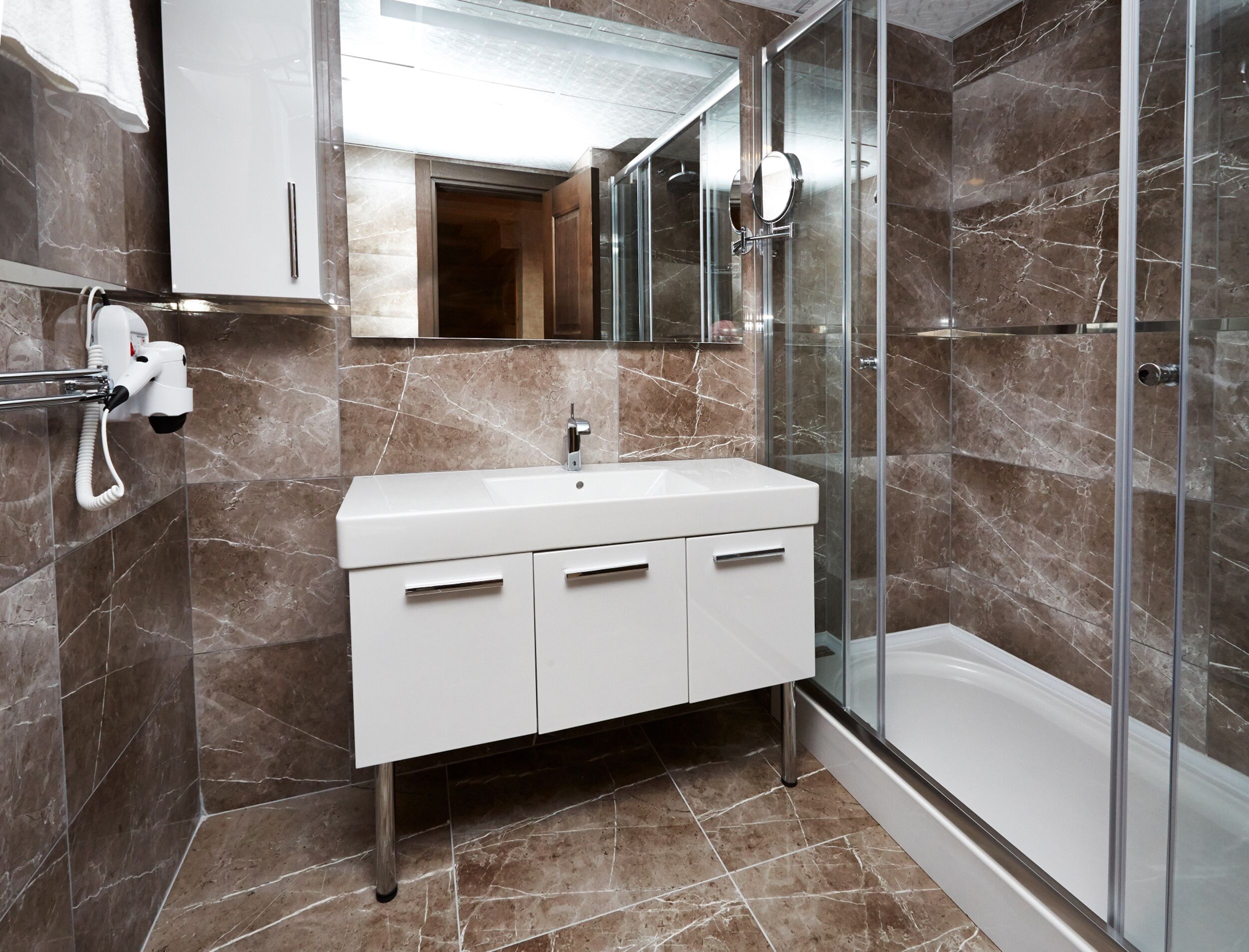 A modern bathroom with a white vanity, a glass shower enclosure, and marble flooring.