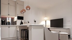 Una cocina moderna con armarios blancos, una isla central con taburetes, un televisor de pantalla plana e iluminación colgante.