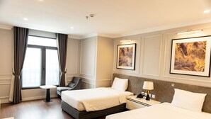 Habitación de hotel con dos camas, una mesita, una silla y obras de arte en las paredes.