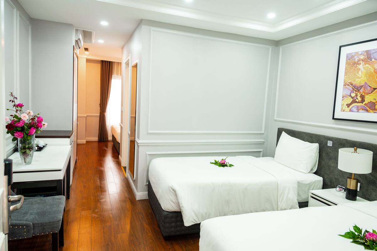 Habitación de hotel con dos camas, un escritorio, una silla, una lámpara y un cuadro en la pared.