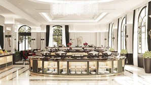 Un lobby de hotel lujoso con una zona de bufé central, elegantes candelabros y grandes ventanales que ofrecen luz natural.