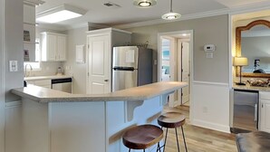 A modern kitchen with white cabinetry, a granite countertop, and a built-in island with bar stools. - Lighthouse Point 6C | Pool Views, Beach Access! (Tybee Island)