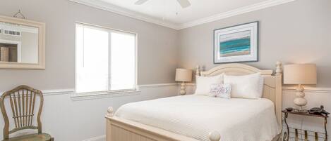 A bedroom with a bed, a chair, a nightstand, a ceiling fan, a window, and a framed picture on the wall.
