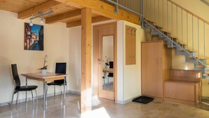 Ein Zimmer mit Holzboden, einer Treppe, einem Schreibtisch mit Stuhl und einer Tür zu einem anderen Raum.