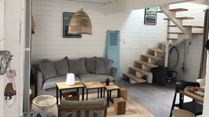 Un salon chaleureux avec un canapé gris, des tables en bois, un luminaire suspendu et un escalier avec des marches en bois.