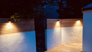 Une terrasse en bois avec un mur blanc et un mur bleu, tous deux dotés de lambris horizontaux en bois et de petites lumières.