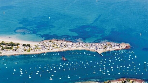 Une vue aérienne d’une zone côtière, avec une plage très fréquentée et de nombreux bateaux sur l’eau.