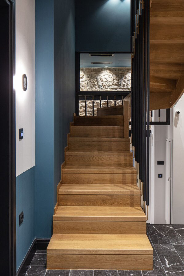 A wooden staircase with a modern design, leading to a room with a stone wall and a view of the outdoors.