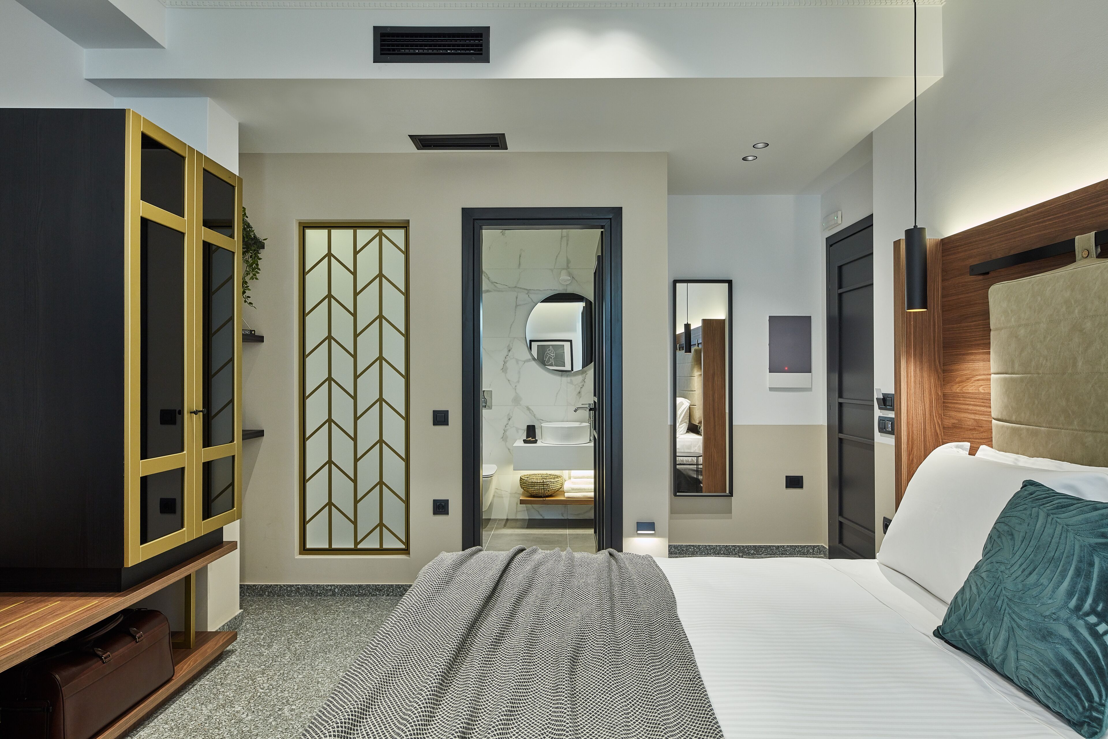 A modern hotel room with a large bed, a wardrobe, a mirror, and a bathroom visible through an open door.