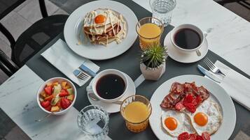A breakfast table with plates of eggs, bacon, pancakes, and fruit, along with cups of coffee and juice.