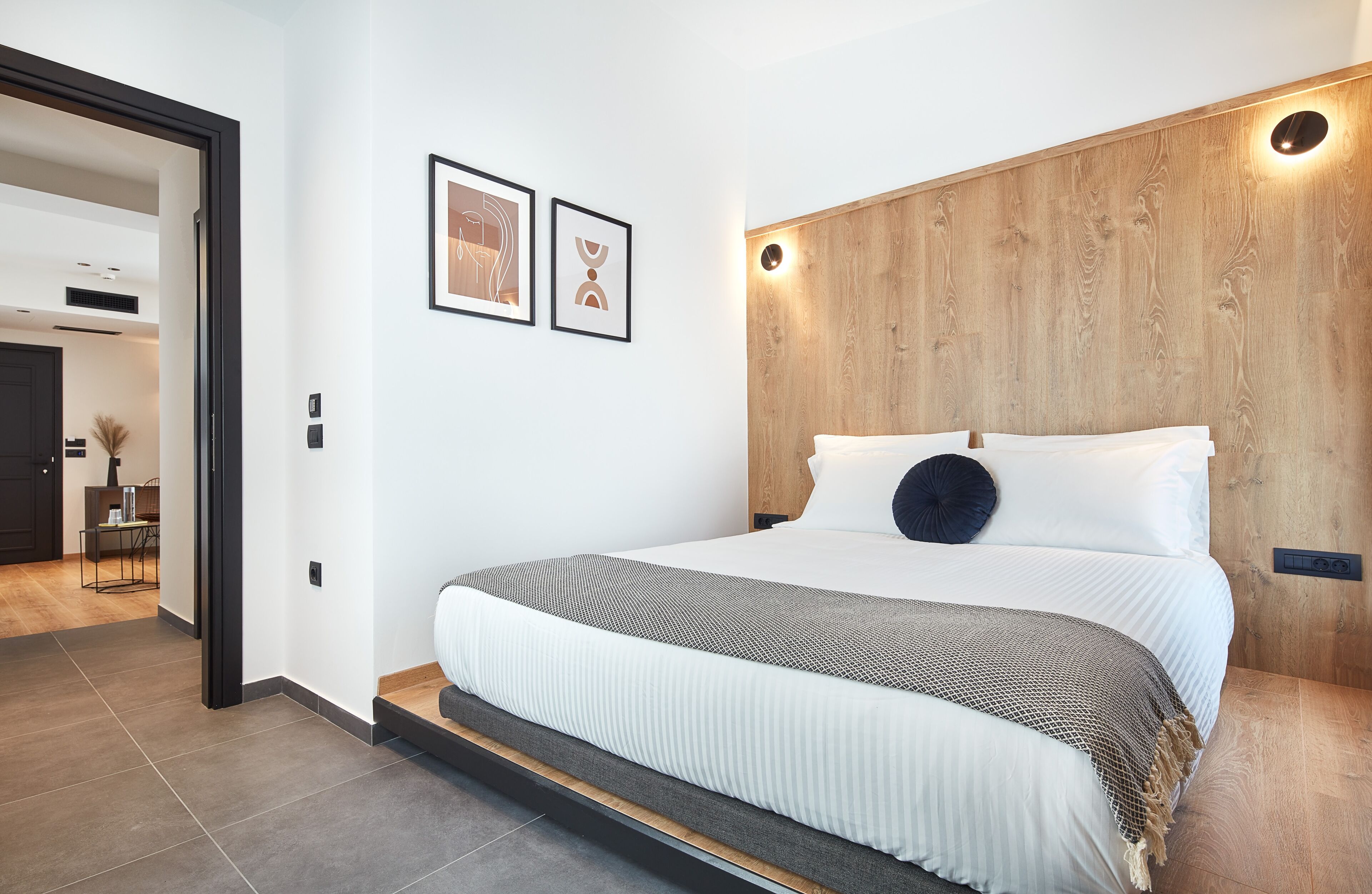 A modern bedroom with a wooden headboard, a large bed with white bedding, and two framed artworks on the wall.