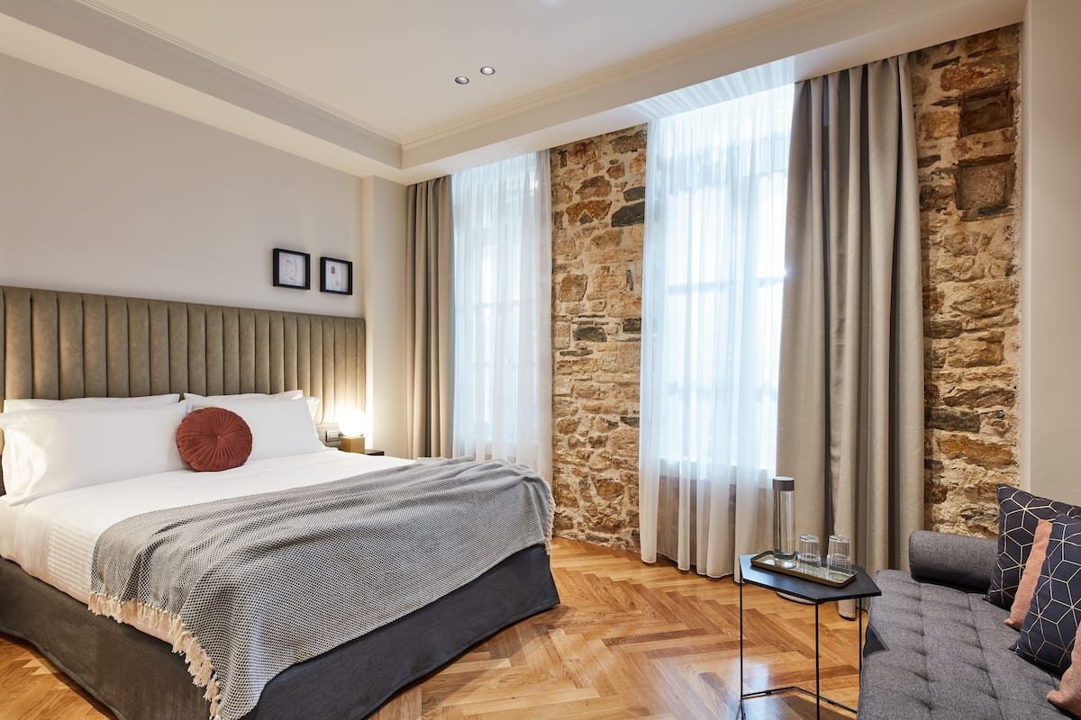 Une chambre à coucher moderne avec un grand lit, un mur décoratif en pierre et une vue sur l’extérieur.