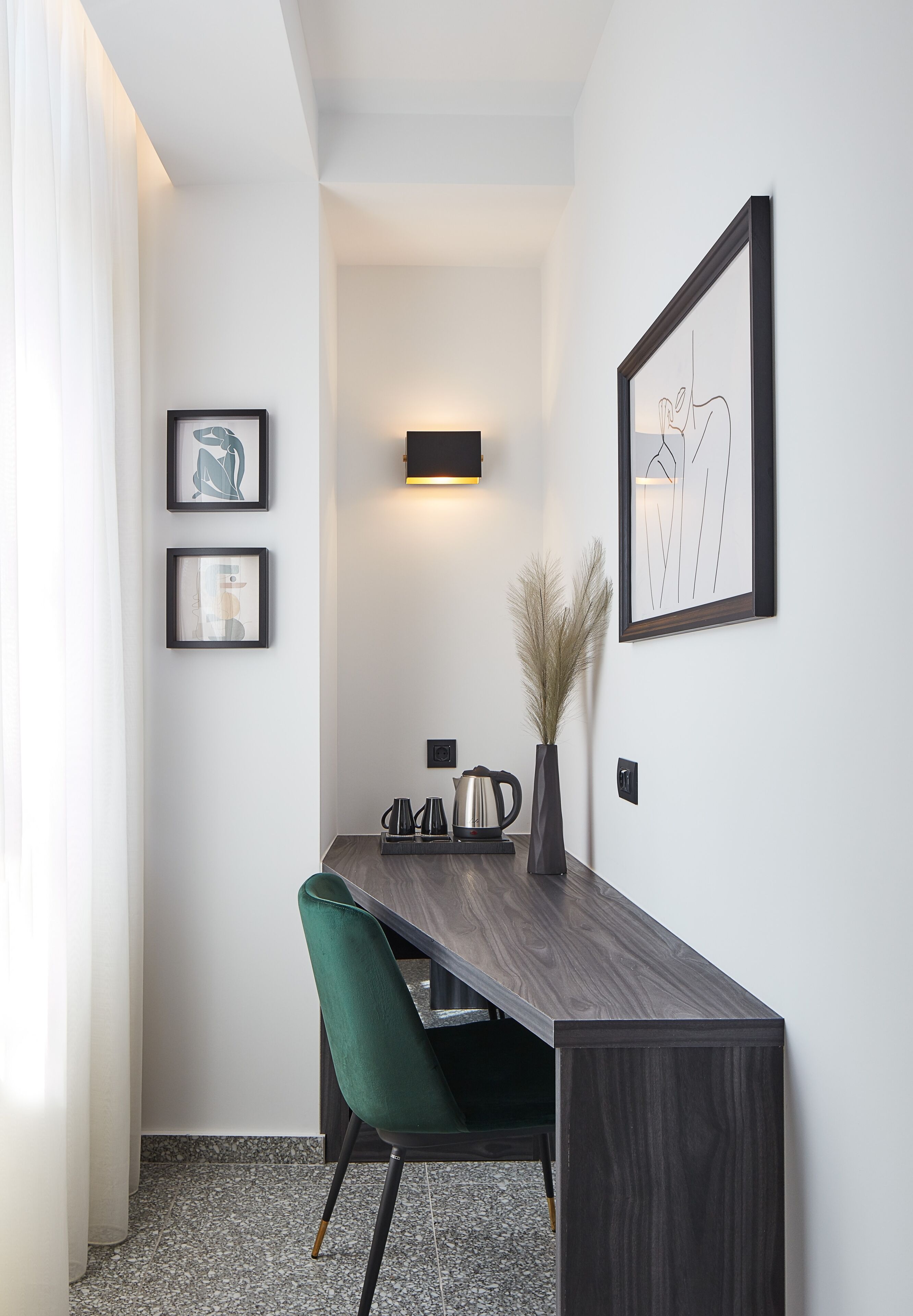Un espace repas moderne avec une table en bois foncé, une chaise recouverte d’un tissu vert et un vase contenant des plumes d’herbe des pampas. Des œuvres d’art encadrées ornent le mur, ainsi qu’un luminaire fixé au mur.