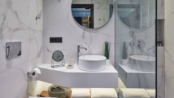 Un baño moderno con un inodoro blanco, un espejo redondo, un lavabo blanco y una zona de ducha con mampara de vidrio.