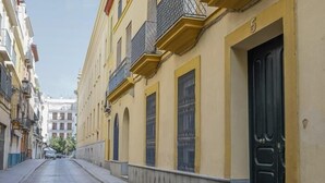 Een smalle straat met keien, geflankeerd door gele gebouwen, met balkonnetjes en een zwarte deur aan de rechterkant.