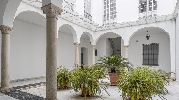 Een binnentuin met witte zuilen, potplanten en een betegelde vloer.