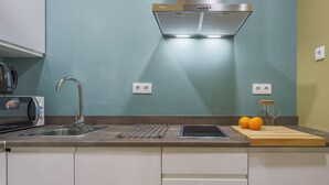 Een moderne keuken met een roestvrijstalen afzuigkap, een ingebouwde gootsteen en een aanrecht met een waterkoker, een broodrooster en een snijplank met sinaasappels.