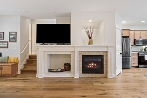 A modern living room with a fireplace, a flat-screen TV, and a staircase leading to another level. - Tranquility On The Bluffs 3 Bedroom Townhouse by RedAwning (Bend)
