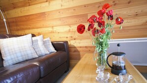 A wooden interior with a brown leather sofa, a glass vase with red flowers, and a coffee maker on a wooden table.