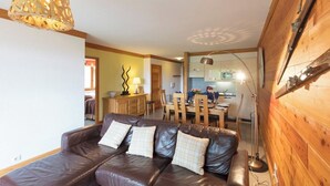 A living room with a leather sofa, wooden dining table, and a kitchen in the background.