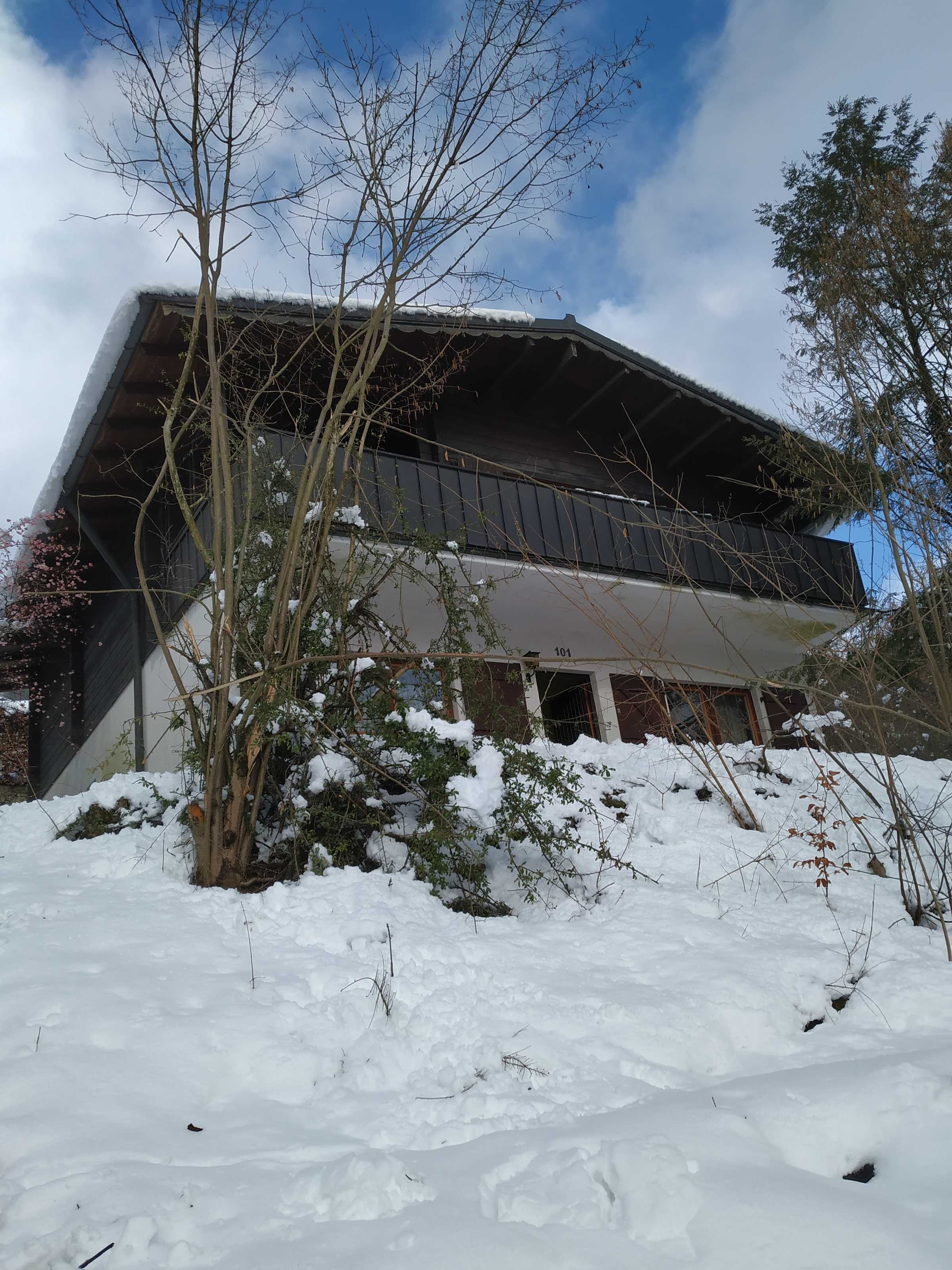 Un bâtiment doté d’un toit en pente, entouré d’un sol enneigé et d’une végétation clairsemée.