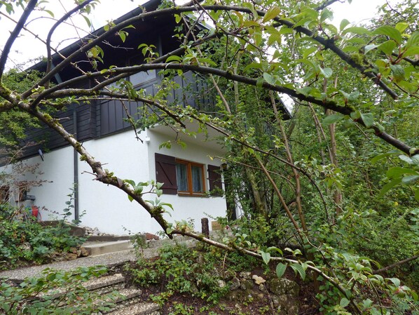 Un bâtiment blanc avec un toit foncé, une porte en bois et une fenêtre avec des volets.