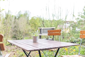 Une table en bois avec des pieds en métal, un seau en métal contenant une plante et deux chaises en bois.