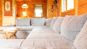 A log cabin interior with a large sectional sofa, a wooden dining table, and a hanging light fixture. - Vacation home Frankenglück - Apartment Holz vor der Hütt'n (Egloffstein)