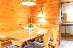 Une table à manger en bois, des chaises, une plante en pot et un luminaire fixé au mur.