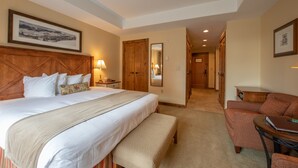 Quarto de hotel com uma cama grande, cabeceira de madeira, um banco, escrivaninha, cadeira e espelho.