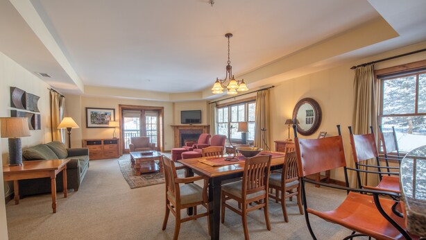 A spacious living room with a wooden dining table, comfortable seating, and a fireplace. - Wheelchair Accessible 2-Bedroom Slopeside Condo - No Cleaning Fee! by RedAwning (Crested Butte)
