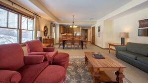 A spacious living room with a wooden coffee table, red armchairs, and a green sofa. A dining area with a wooden table and chairs is visible in the background. - Wheelchair Accessible 2-Bedroom Slopeside Condo - No Cleaning Fee! by RedAwning (Crested Butte)