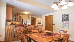 A dining area with wooden chairs and a table, wooden cabinets, a refrigerator, and a welcome sign. - Wheelchair Accessible 2-Bedroom Slopeside Condo - No Cleaning Fee! by RedAwning (Crested Butte)