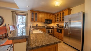 A kitchen with granite countertops, wooden cabinets, stainless steel appliances, and a window with curtains. - Wheelchair Accessible 2-Bedroom Slopeside Condo - No Cleaning Fee! by RedAwning (Crested Butte)