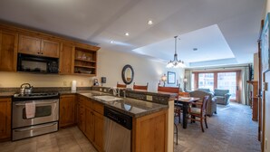 A spacious kitchen with wooden cabinets, a built-in microwave, and a dishwasher. There is a dining area with a table and chairs, and a large window providing natural light.