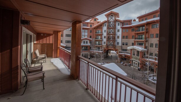 A balcony with wooden railings, a covered area, and a view of multi-story buildings with balconies.