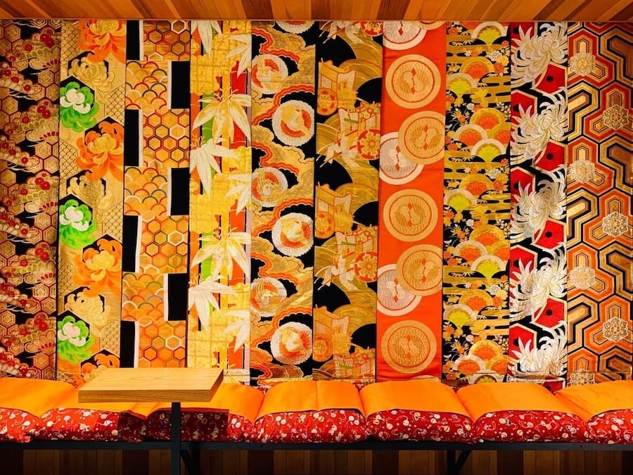 A room with a traditional Japanese tatami mat floor, a wooden table, and a wall decorated with various colorful patterns.