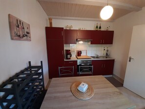 A compact kitchen with red cabinets, a wooden table, and a hanging light fixture.
