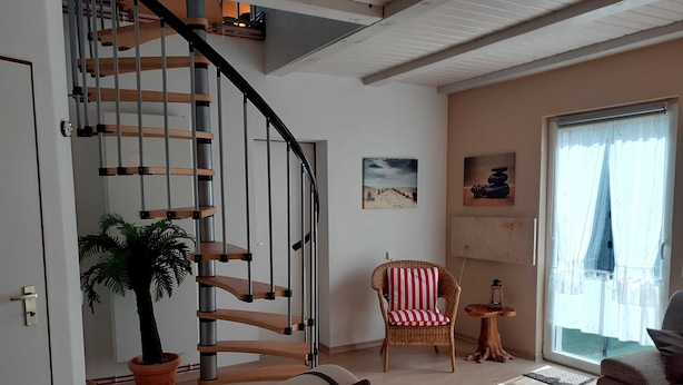 Una sala moderna con una escalera espiral, una planta en maceta, un sillón a rayas y un sofá.