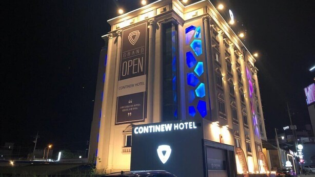 La façade de l’hôtel Continew la nuit, avec ses enseignes illuminées et une grande banderole annonçant son « inauguration officielle ».