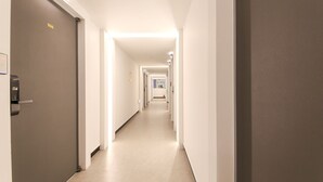 Un couloir d’hôtel au design moderne, avec un long couloir bordé de portes des deux côtés, un sol plat et un éclairage au plafond lumineux.